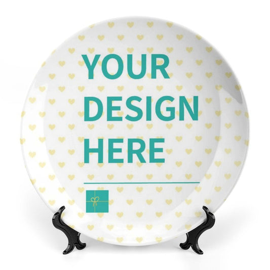Customizable ceramic plate with "YOUR DESIGN HERE" and heart pattern on a stand, a personalized gift.