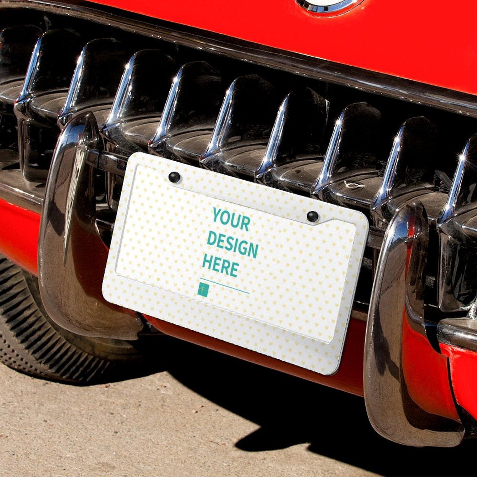 Customizable aluminum license plate with 'YOUR DESIGN HERE' text on classic red car bumper. Heart pattern design.
