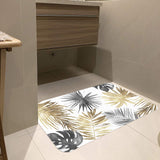 Tropical leaves doormat with gold, gray, and black leaves, indoor/outdoor rubber mat in bathroom setting.