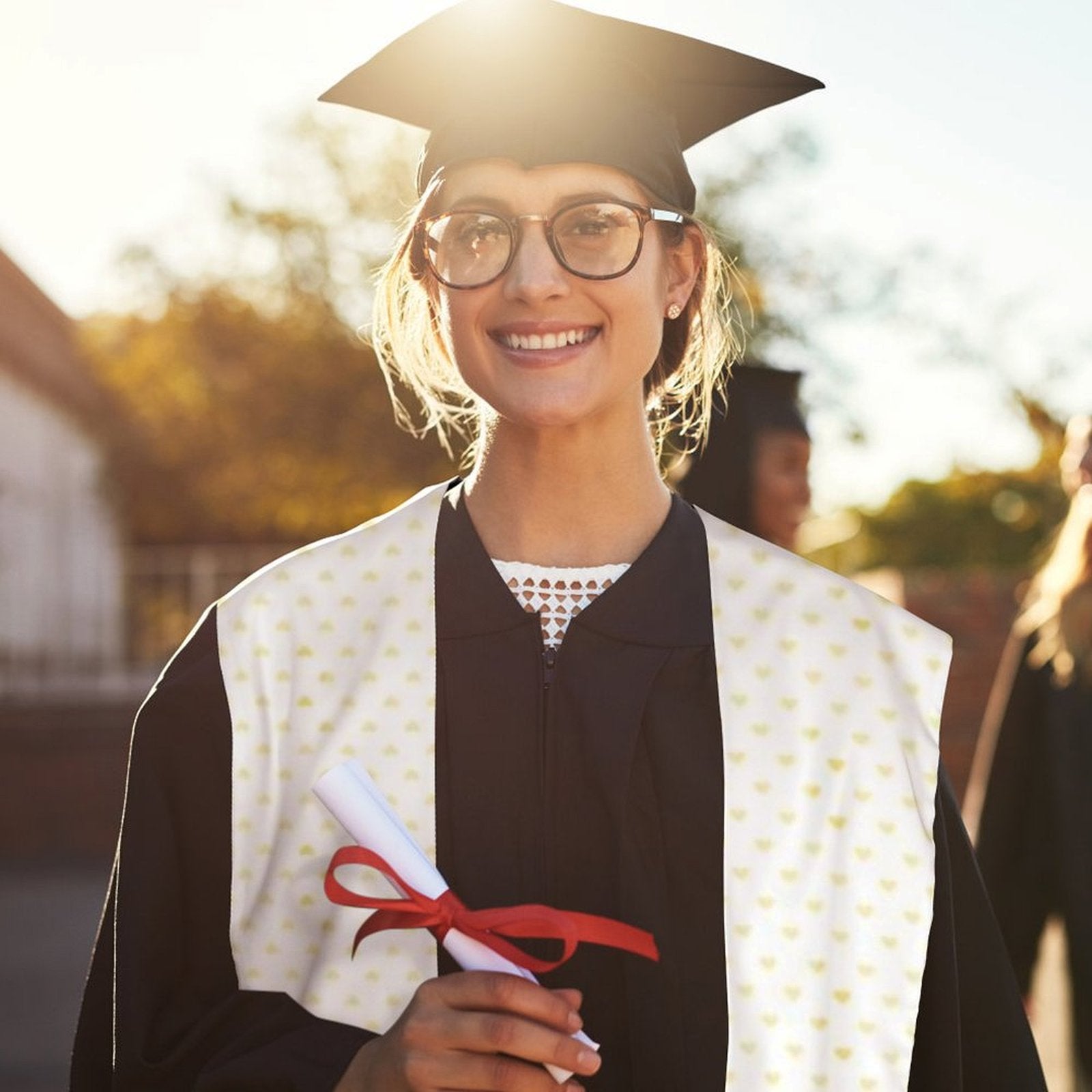 Smiling graduate in cap and gown with personalized graduation stole, holding diploma, perfect senior gift.