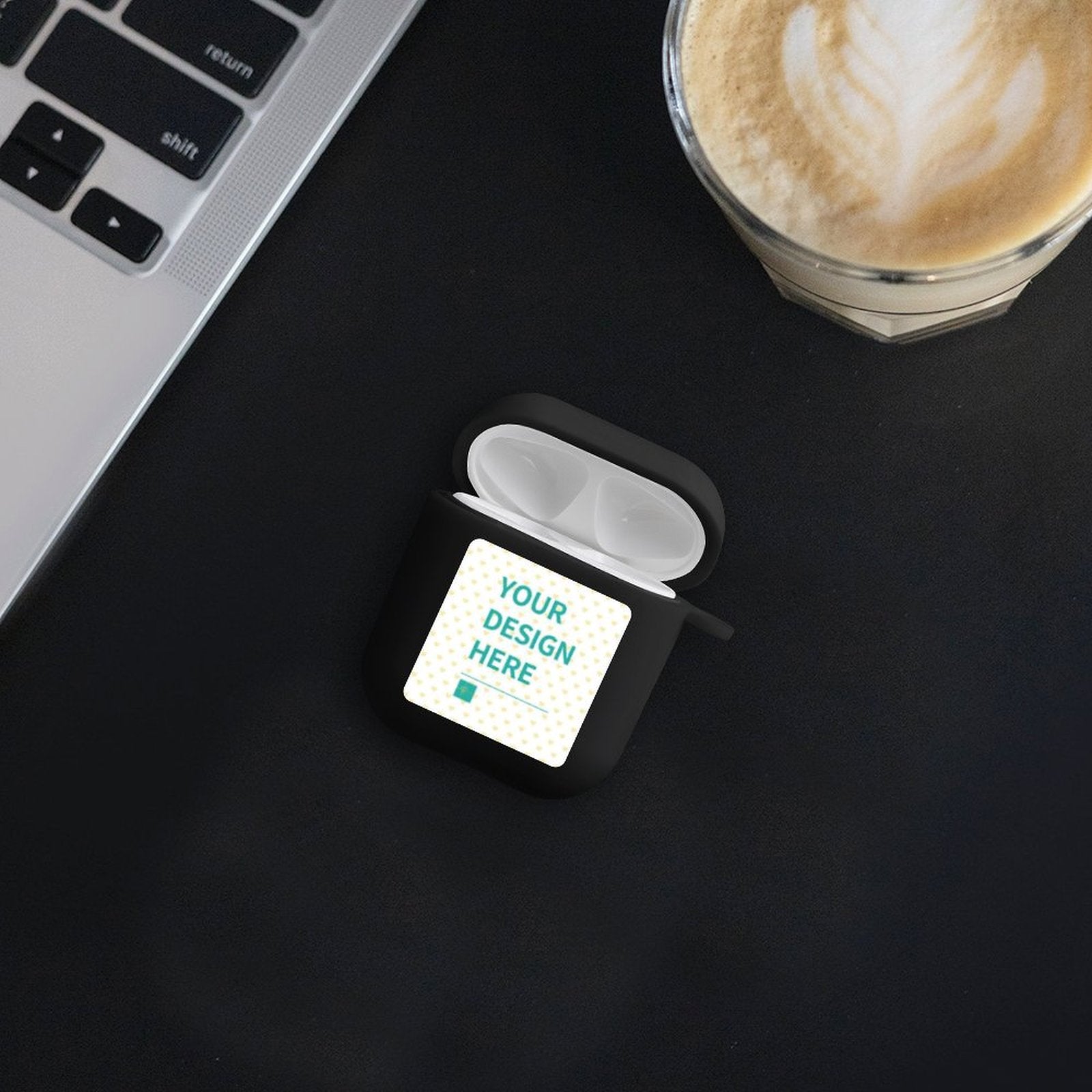 Custom black AirPods case with personalized design area, 'Your Design Here' text, on black surface, laptop and coffee