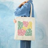 Canvas tote bag with Monstera leaf print in pink, green, and yellow. Eco-friendly cotton shopping bag for women.