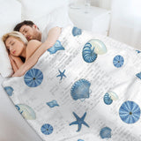 Navy shells pattern fleece blanket on bed, with seashell and starfish design, for cozy bed or sofa, features French text.