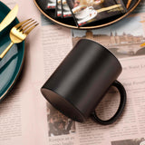 Black ceramic color-changing mug with gold utensils and newsprint background, perfect for coffee or personalized designs.