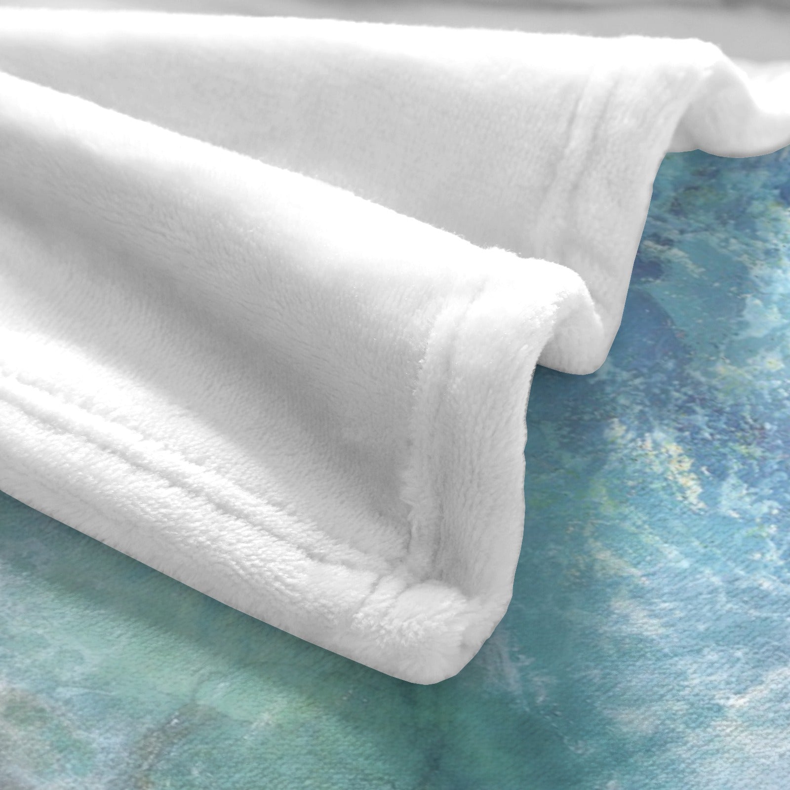 Close-up of a soft white fleece blanket with a blue ocean beach wave design, perfect for couch or bed.
