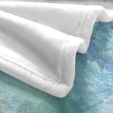 Close-up of a soft white fleece blanket with a blue ocean beach wave design, perfect for couch or bed.