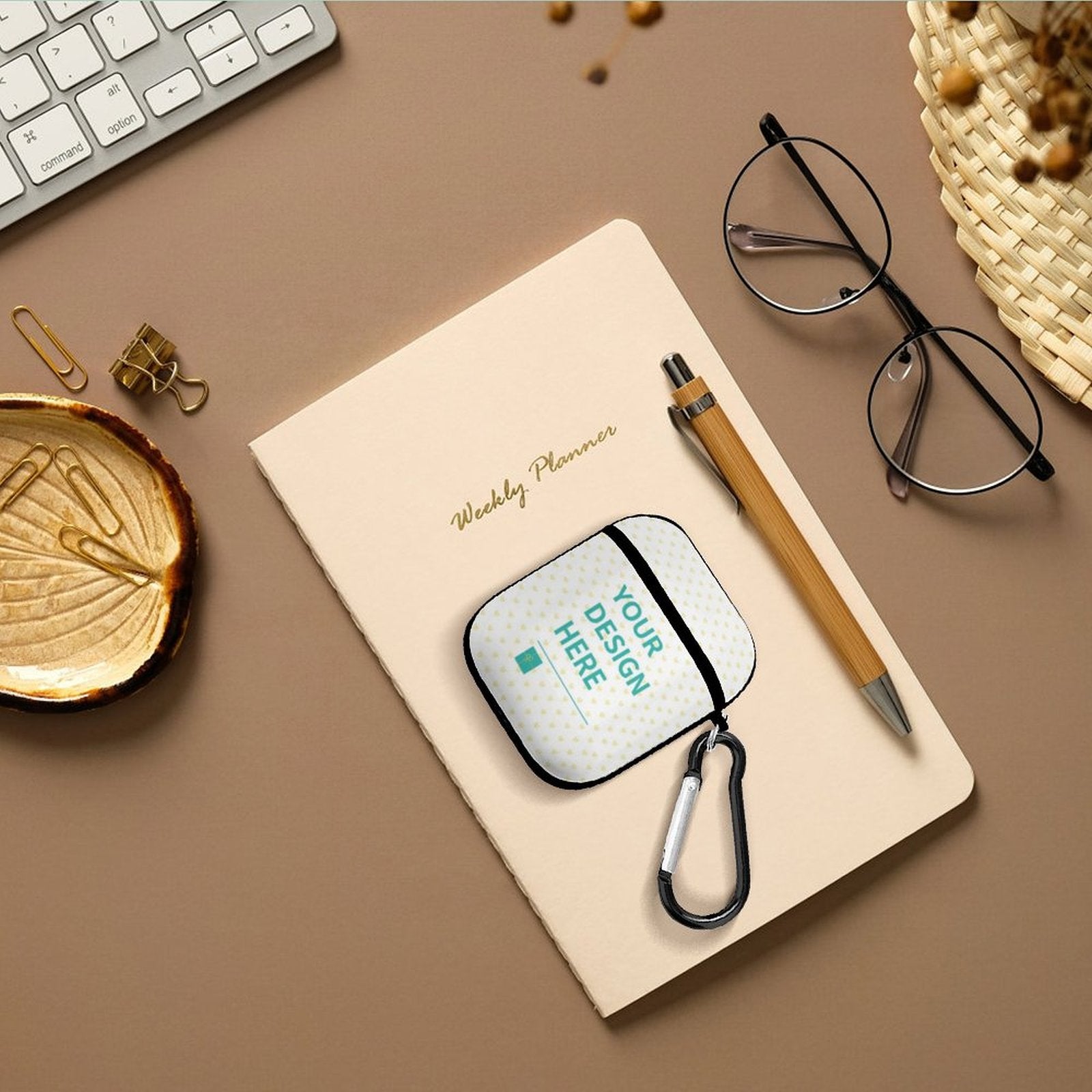 Custom AirPods case with 'YOUR DESIGN HERE' text, PC hard shell with carabiner, on a notebook