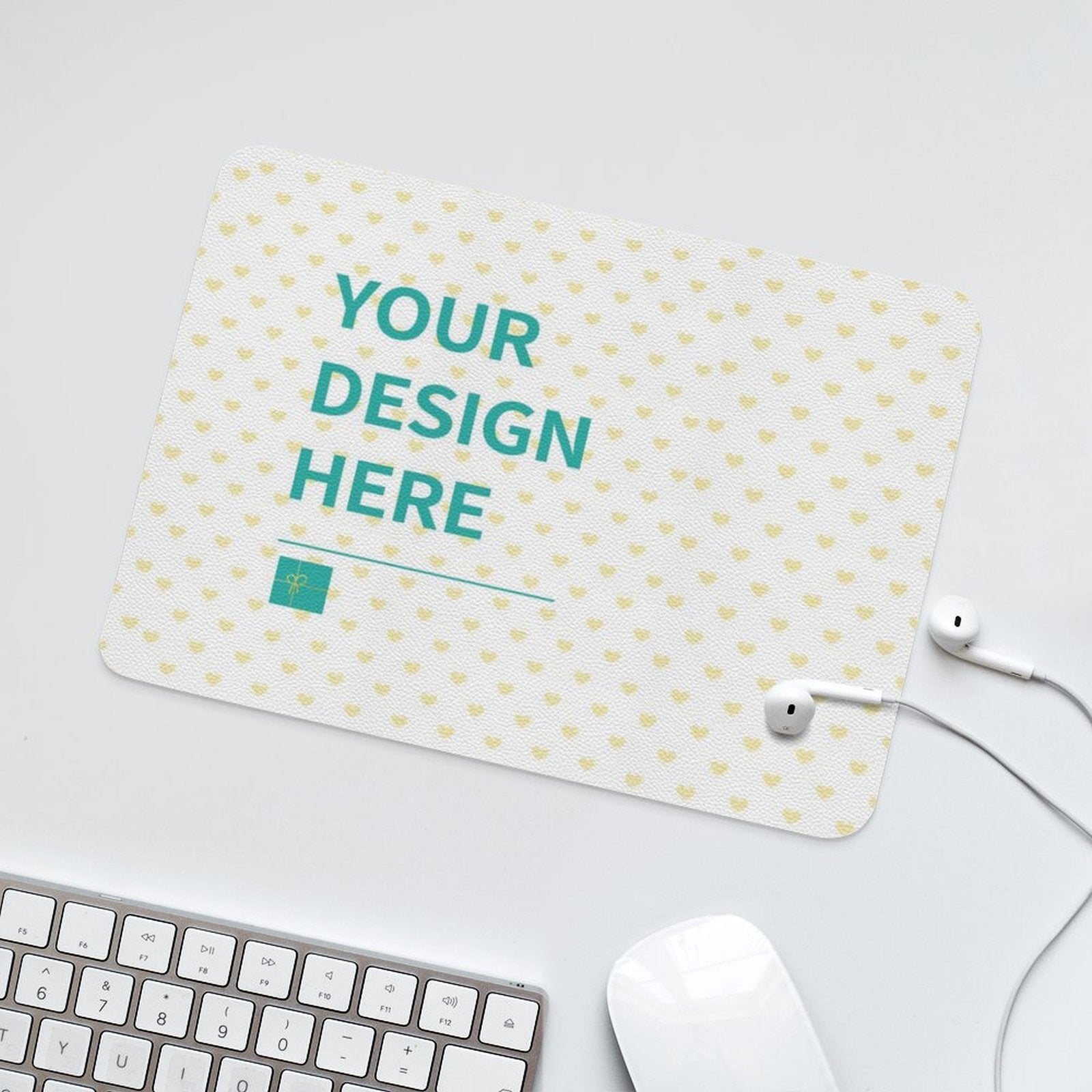Custom desk mat with "YOUR DESIGN HERE" text, white mouse, keyboard, and earbuds, office accessory