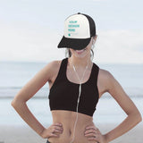 Customizable trucker hat with 'YOUR DESIGN HERE' text, black bill, and mesh back on a woman by the beach.