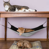 Pet hammock for cats and small dogs, black and gray hanging bed under a table, with a resting cat and a dog.