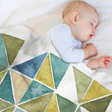 Geometric fleece blanket with sleeping baby. Soft lamb wool, green, blue, and beige triangles, perfect for bed and travel.