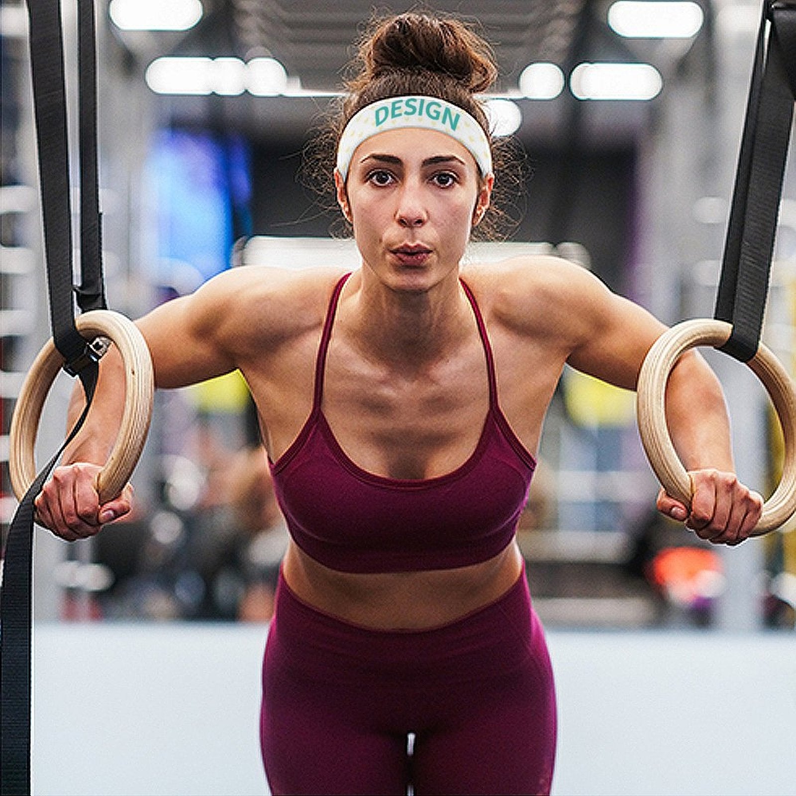 Woman wearing a 'DESIGN' sports headband, working out with gymnastic rings at gym