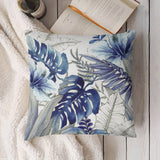 Blue tropical leaf pillow cover; soft, decorative design with watercolor leaves and flowers; placed on a white blanket.