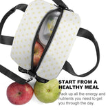 Reusable lunch bag with yellow heart pattern, black handle, and fresh fruits inside, perfect for a healthy meal on the go.