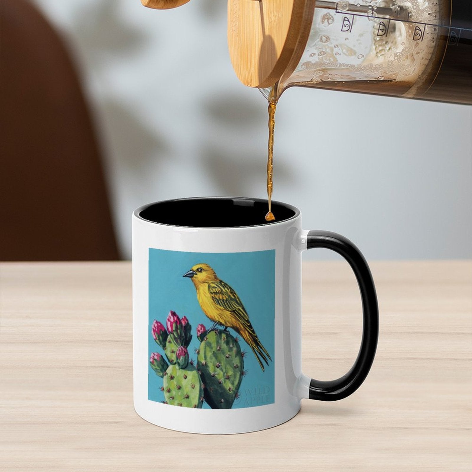 White ceramic mug with black interior and handle, featuring a yellow bird and cactus design, by WILD APPLE