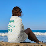 Custom beach towel with YOUR DESIGN HERE on a person sitting on the beach. Personalized beach accessory.