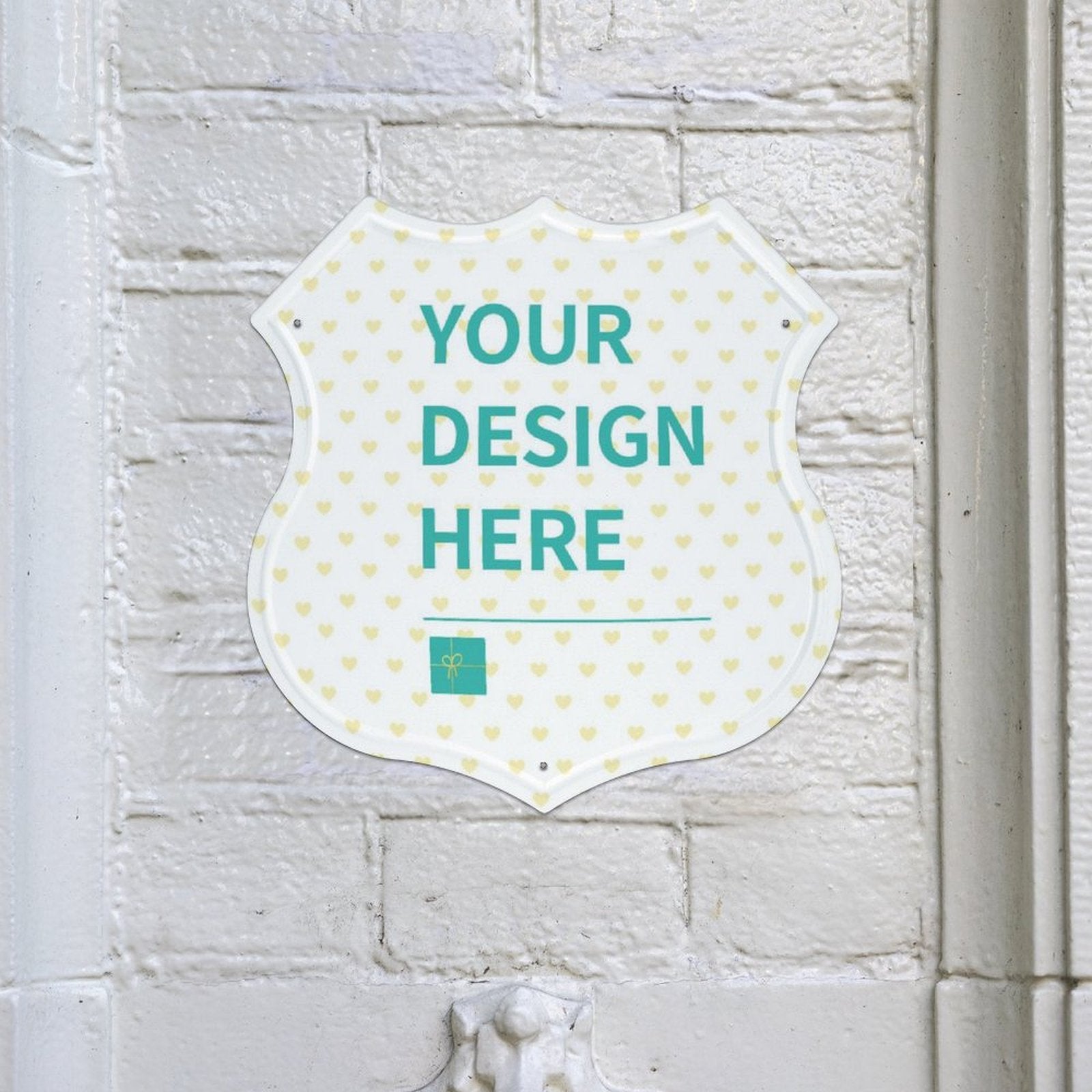 Customizable shield-shaped metal sign with 'YOUR DESIGN HERE' on white brick wall, perfect for shop decor.