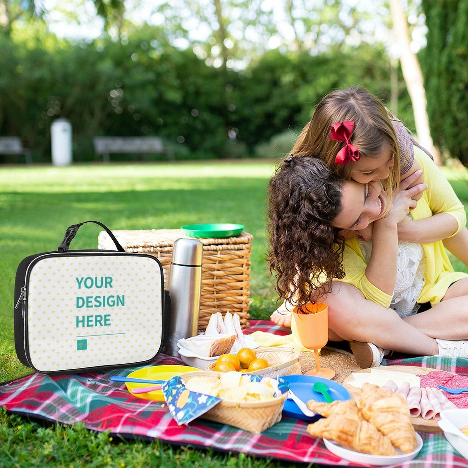 Customizable lunch bag for work or picnic with 'Your Design Here' text; family picnic in park setting