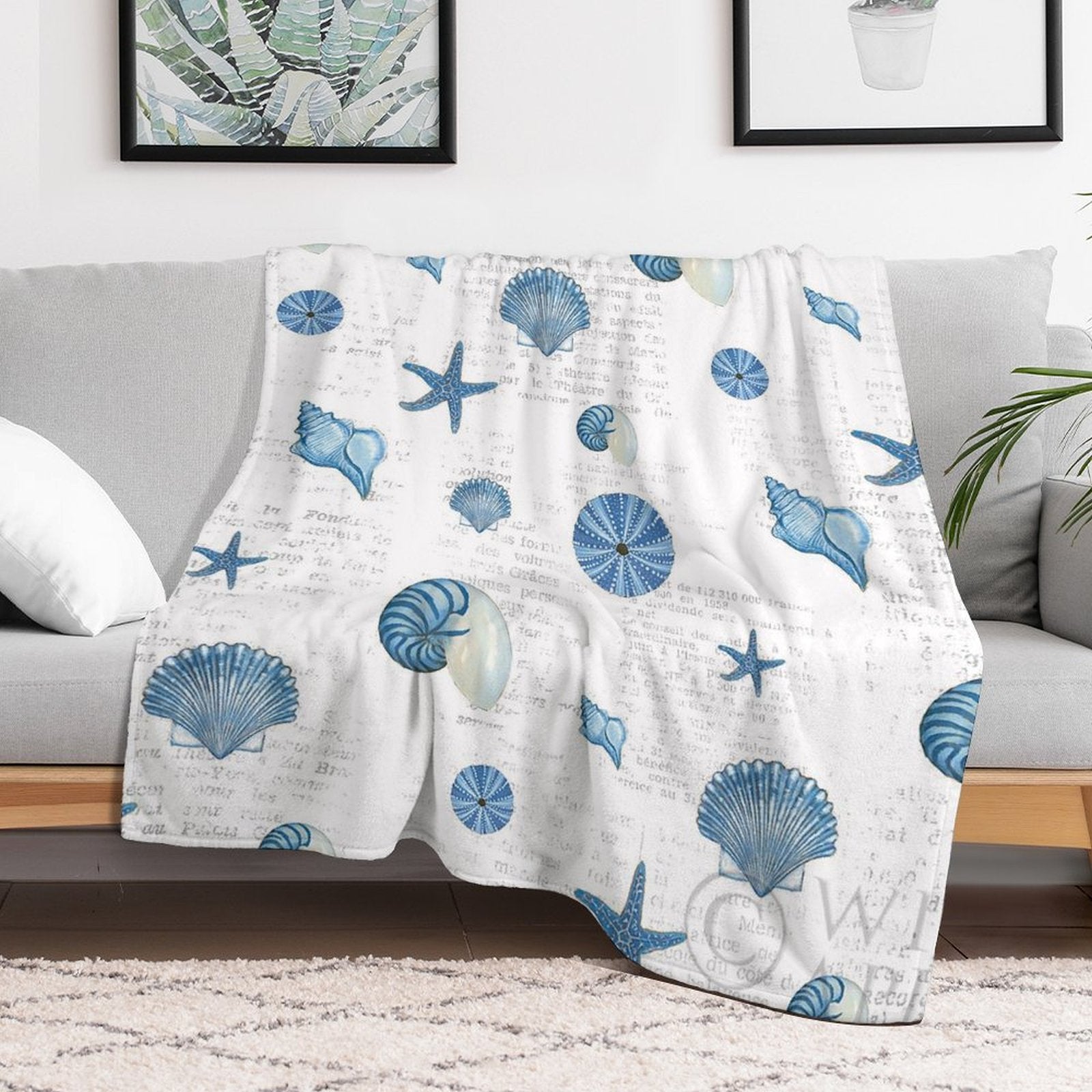 Navy shells pattern fleece blanket on sofa, featuring blue seashells and starfish design, cozy bed or sofa blanket.