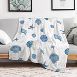 Navy shells pattern fleece blanket on sofa, featuring blue seashells and starfish design, cozy bed or sofa blanket.